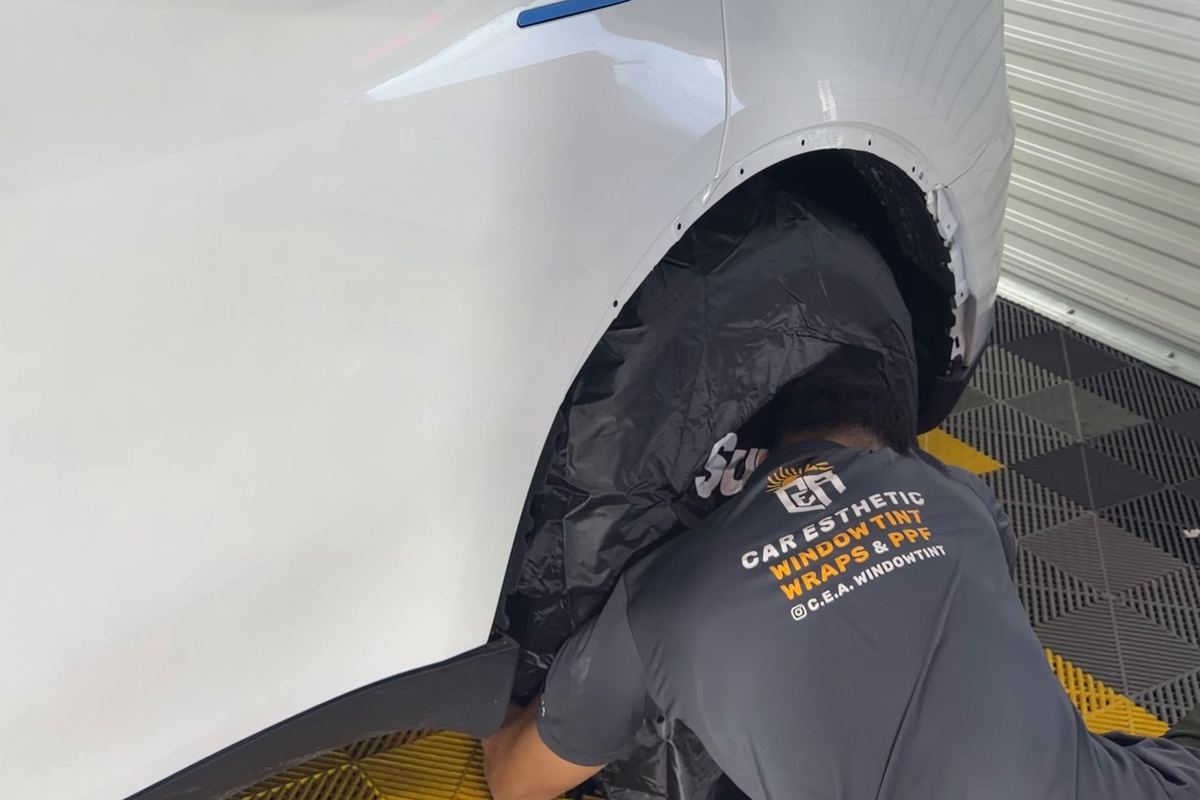 Installer working on the lower rear panel of a white Tesla Model Y