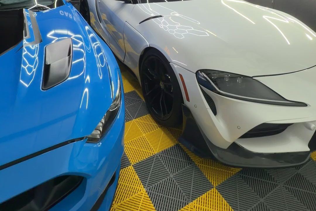 White Toyota GR Supra and a blue sports car on the checkered floor of the CEA bay