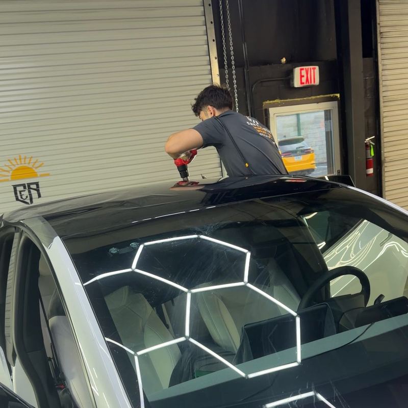Installer using a heat gun on the glass roof of a white Tesla Model Y